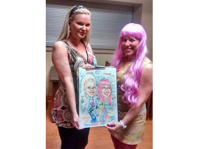 Womans posing next to their Caricature drawing.
